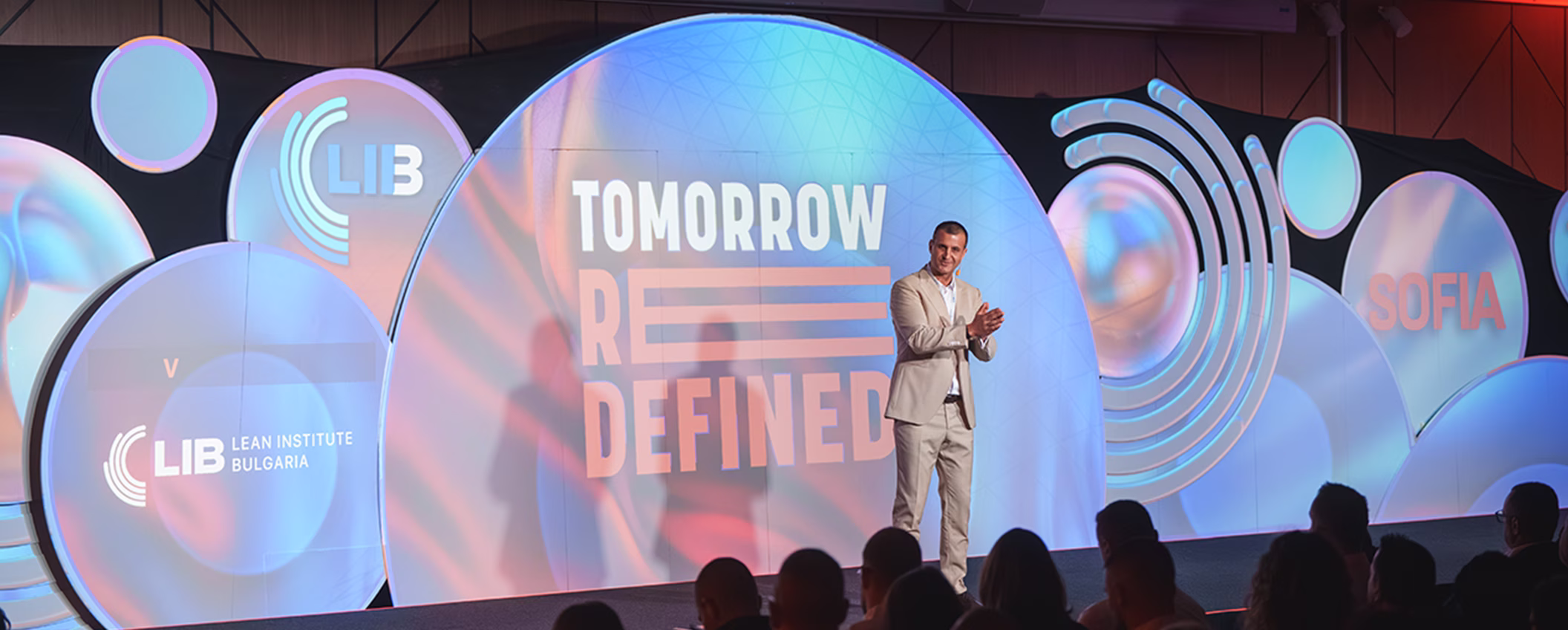 Лектор изнася презентация на модерната брандирана сцена с логото на Lean Institute Bulgaria и Tomorrow Redefined.