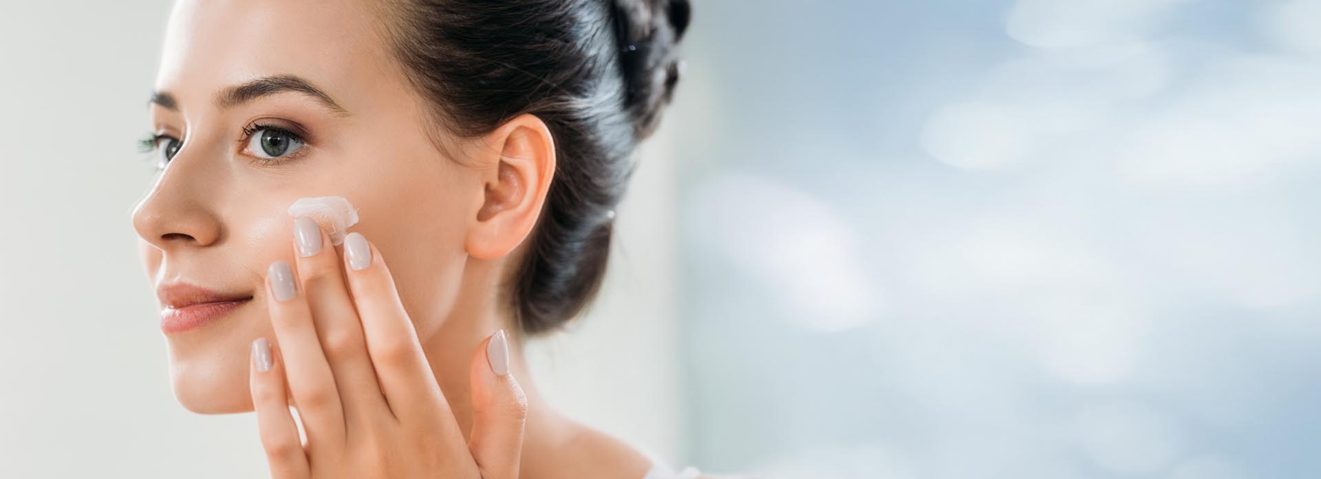 Kvinne som påfører ansiktskrem på venstre kinn med fingrene.