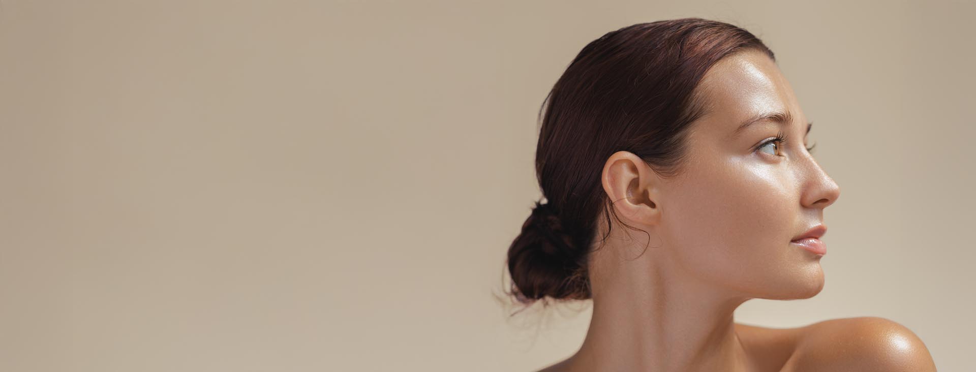 Nærbilde av en kvinne med oppsatt mørkt hår som ser mot høyre mot en nøytral beige bakgrunn.