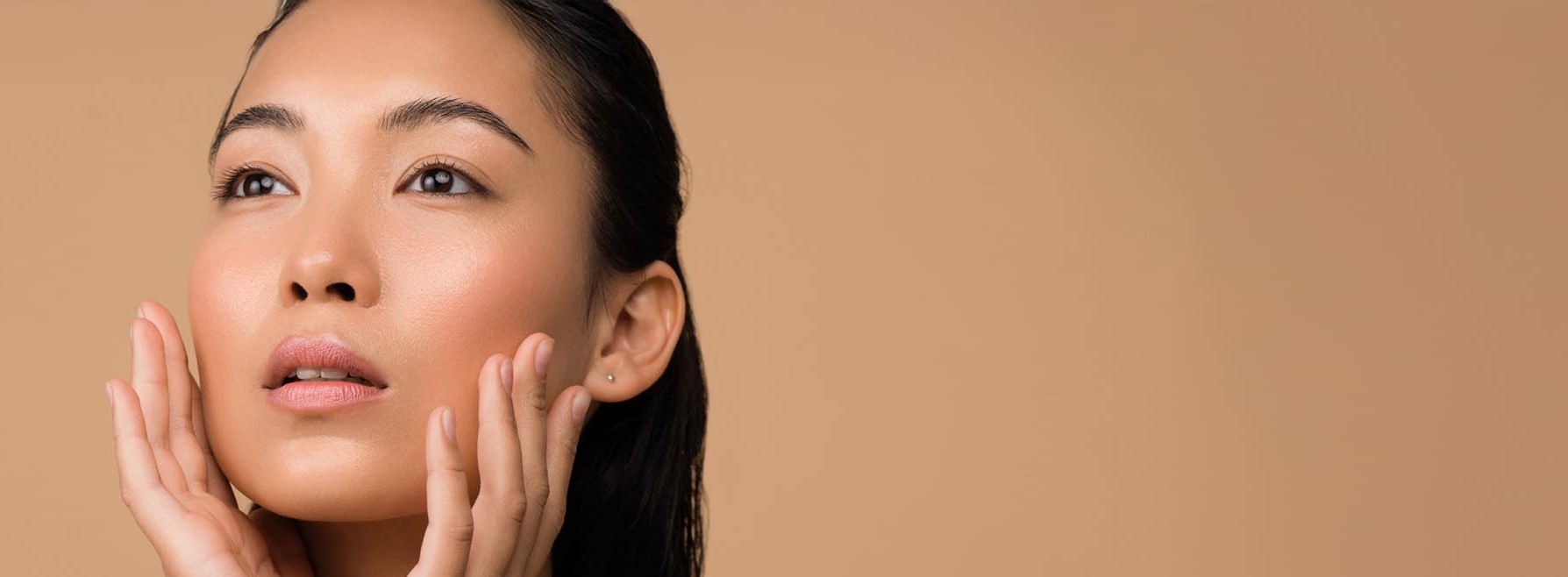 Nærbilde av en kvinne med klar hud som berører ansiktet forsiktig med begge hender.