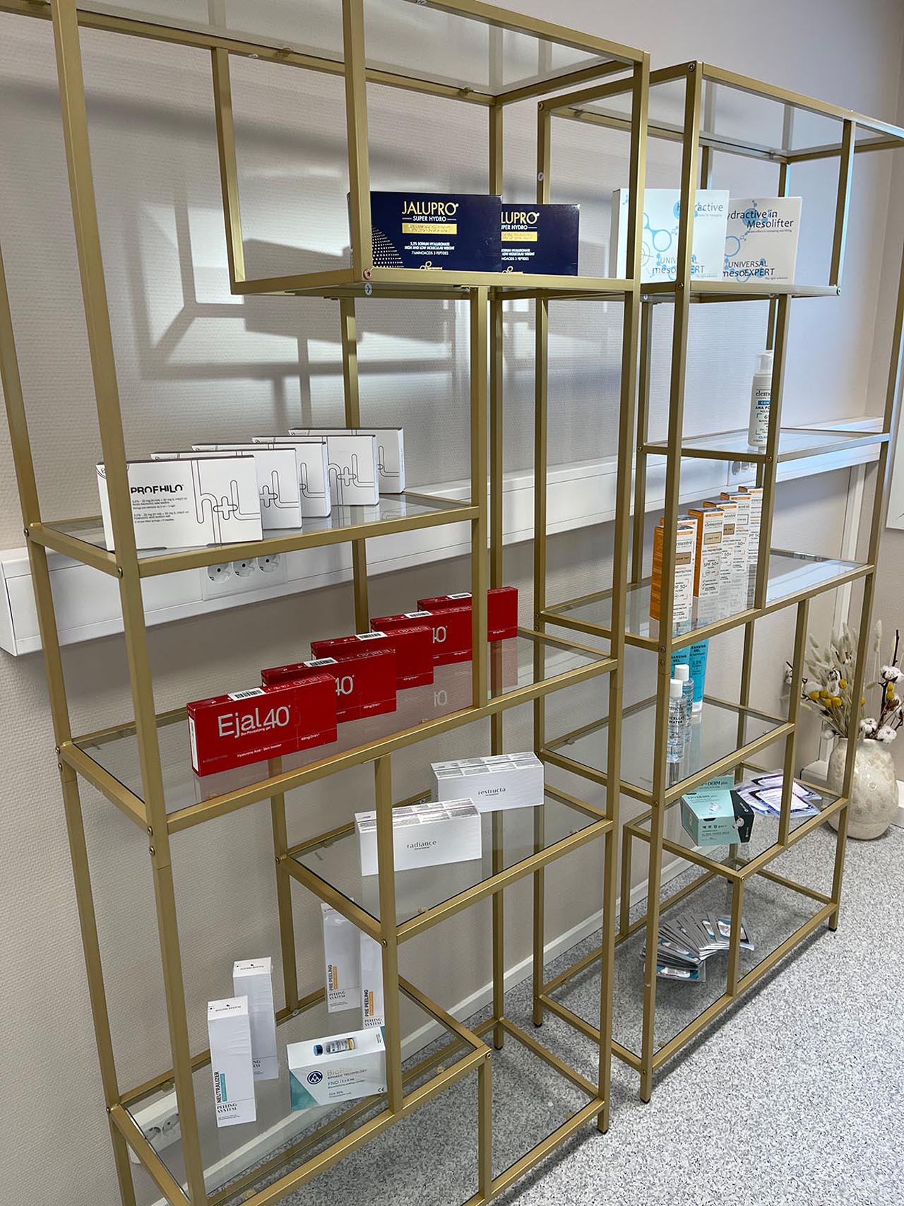 Gullfarget metallhylle med ulike skjønnhets- og hudpleieprodukter i bokser arrangert på glasshyller.