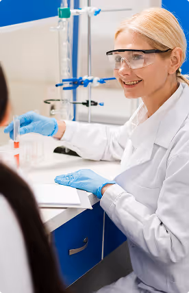 Female scientist wearing safety goggles and gloves holding a test tube in a laboratory setting.