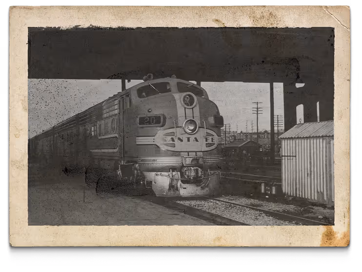 Vintage black and white photo of a Santa Fe locomotive train at a station platform under a large overhang.