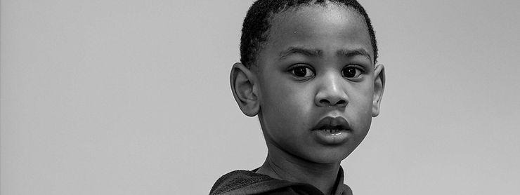 Sur un fond gris un enfant d'origine africaine nous regarde dans les yeux, son regard est profond et émouvant.