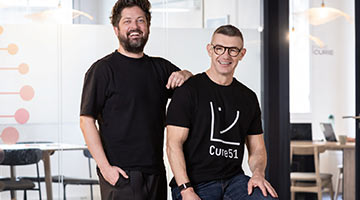 Deux hommes souriants posent dans les bureaux de Cure51.
