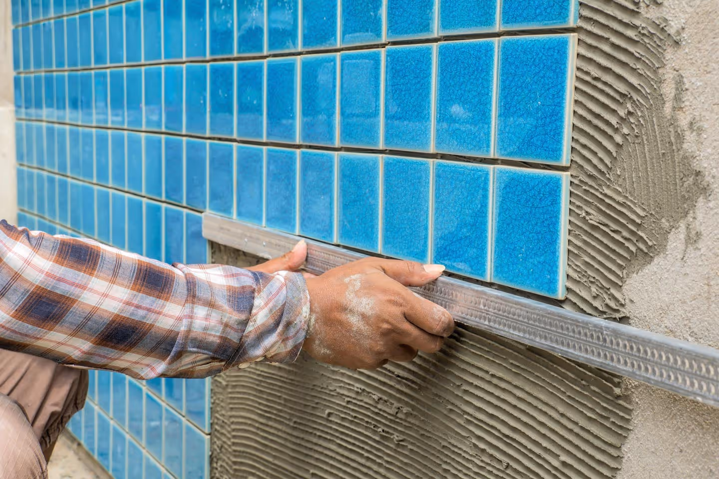Close-up of a person installing blue ceramic tiles on a wall using a leveling tool.