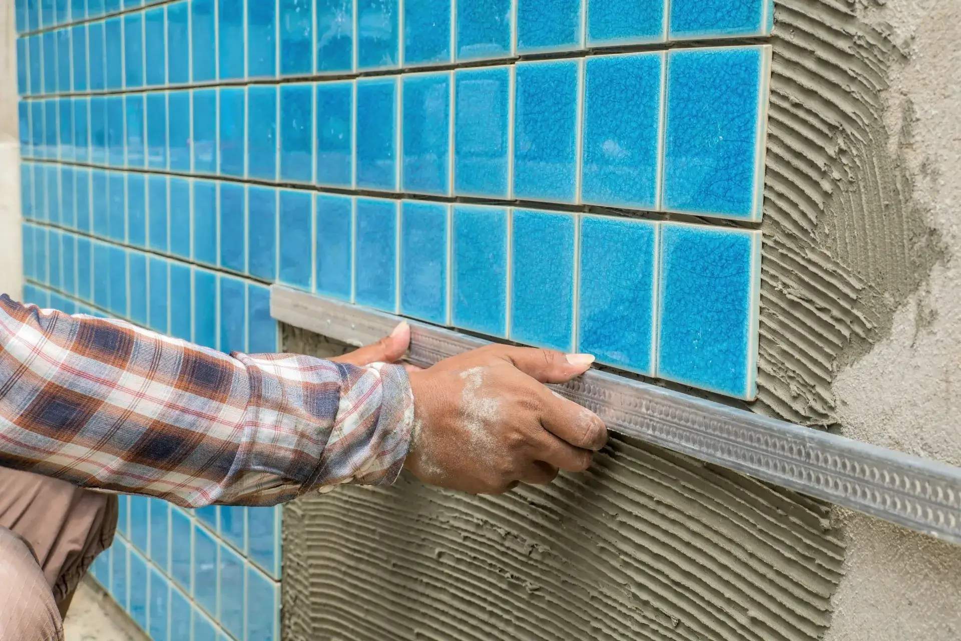 Close-up of a person installing blue ceramic tiles on a wall using a leveling tool.