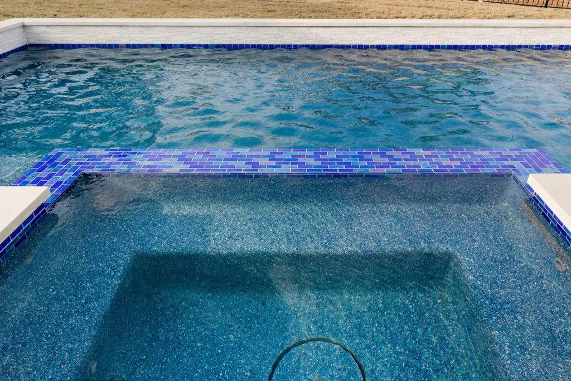 A section of a swimming pool showing clear blue water with a tiled edge and a shallow area in the foreground.