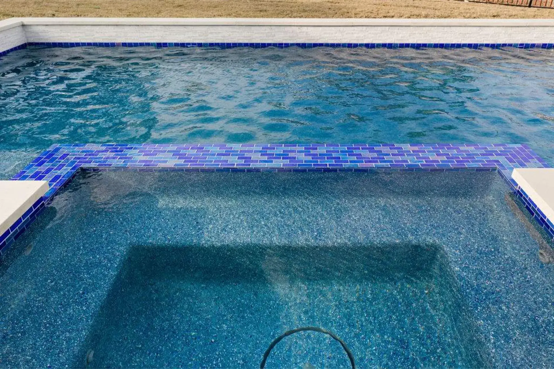 A section of a swimming pool showing clear blue water with a tiled edge and a shallow area in the foreground.