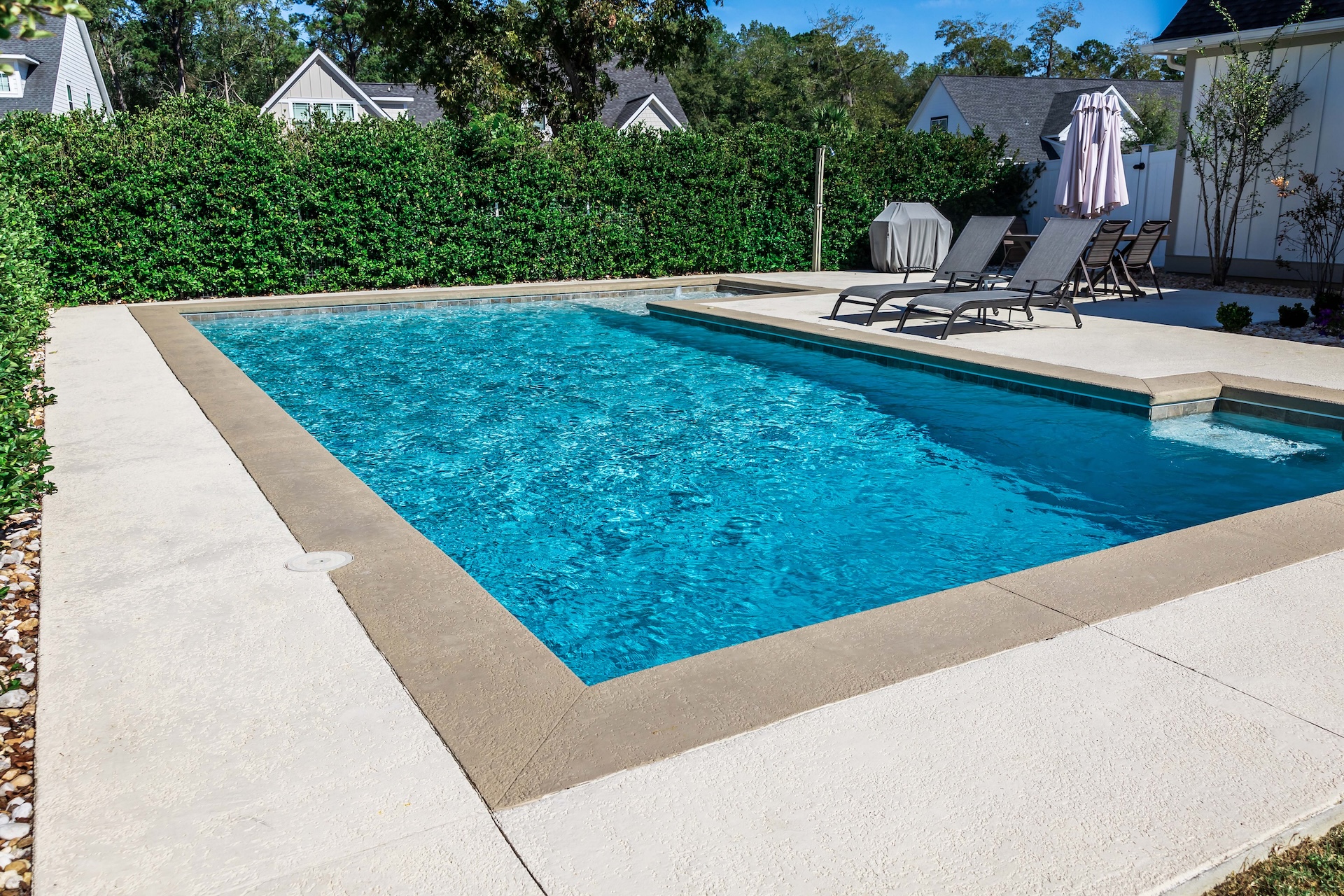 A backyard swimming pool with lounge chairs, umbrellas, and greenery.