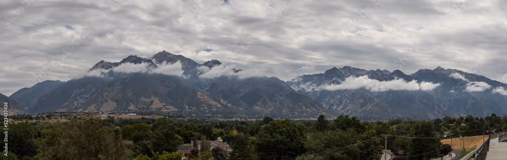 Cloudy sky over a mountain range with low-hanging clouds and forested area below.