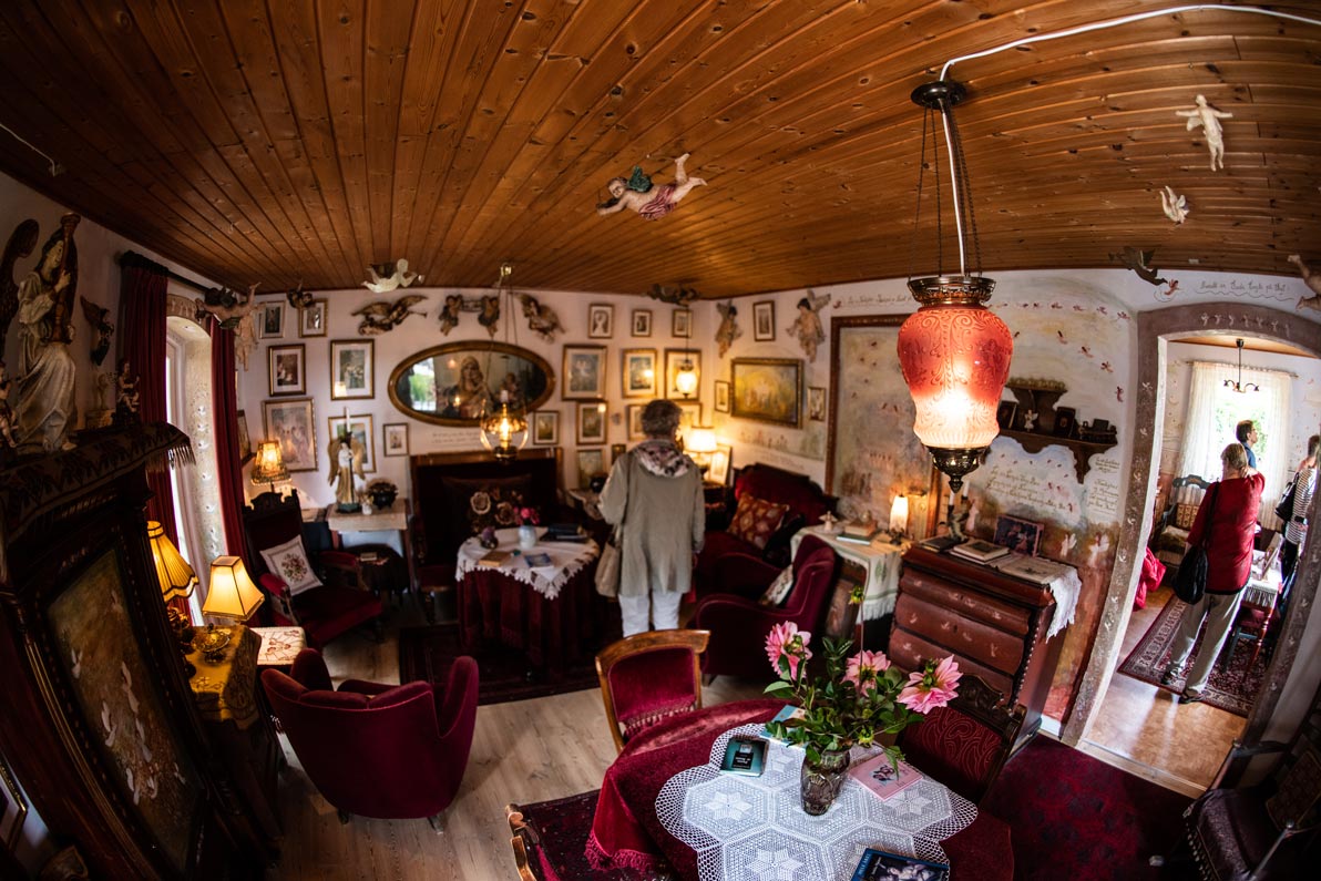 Hyggeligt stueinteriør med træloft, røde møbler, blomster på bordet og dekorative englefigurer på vægge og loft.