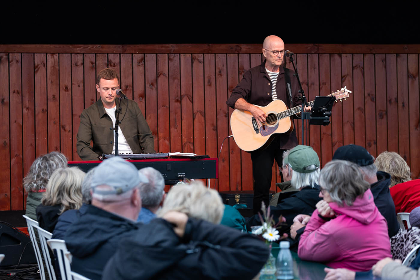 To mænd spiller musik foran et publikum, den ene på keyboard og den anden på akustisk guitar.