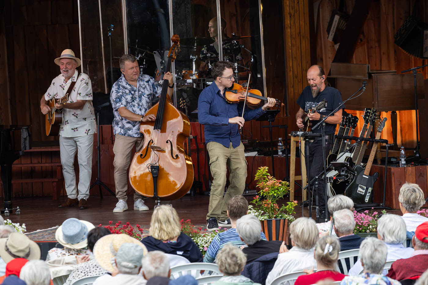 Kvinde i blå kjole synger i mikrofon foran et træpanel med musikudstyr bag hende.