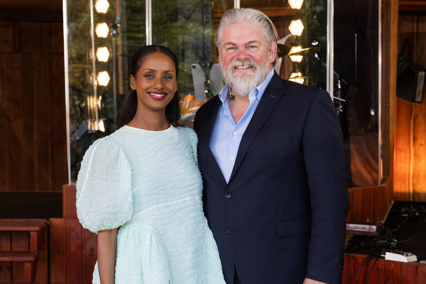 En smilende kvinde i lyseblå kjole med puffede ærmer står ved siden af en smilende mand med gråt skæg og navy blazer.