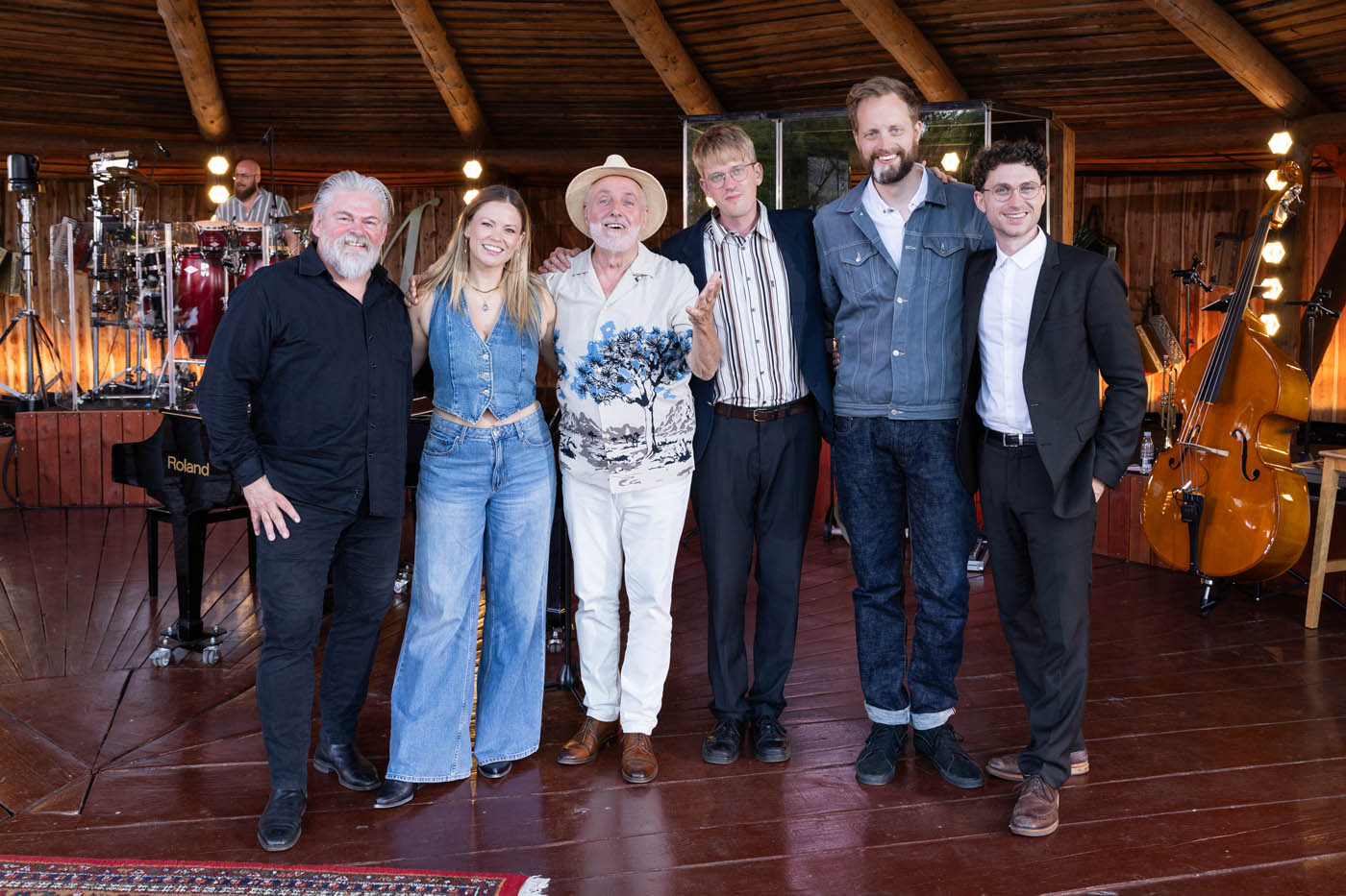 To musikere spiller guitar på en scene foran et stort publikum udendørs under træer.