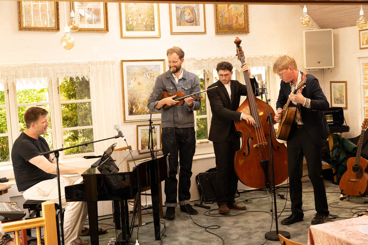 Fire mænd spiller musik sammen indendørs med klaver, violin, kontrabas og guitar.