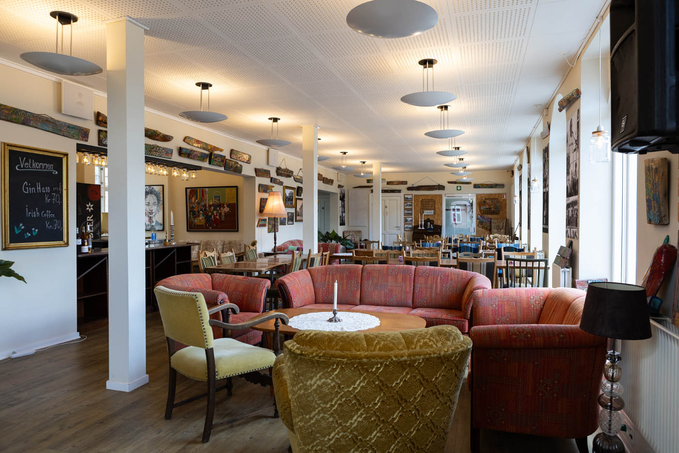 Hyggelig café med farverige sofaer, stole og spiseborde i et lyst rum med kunst på væggene.