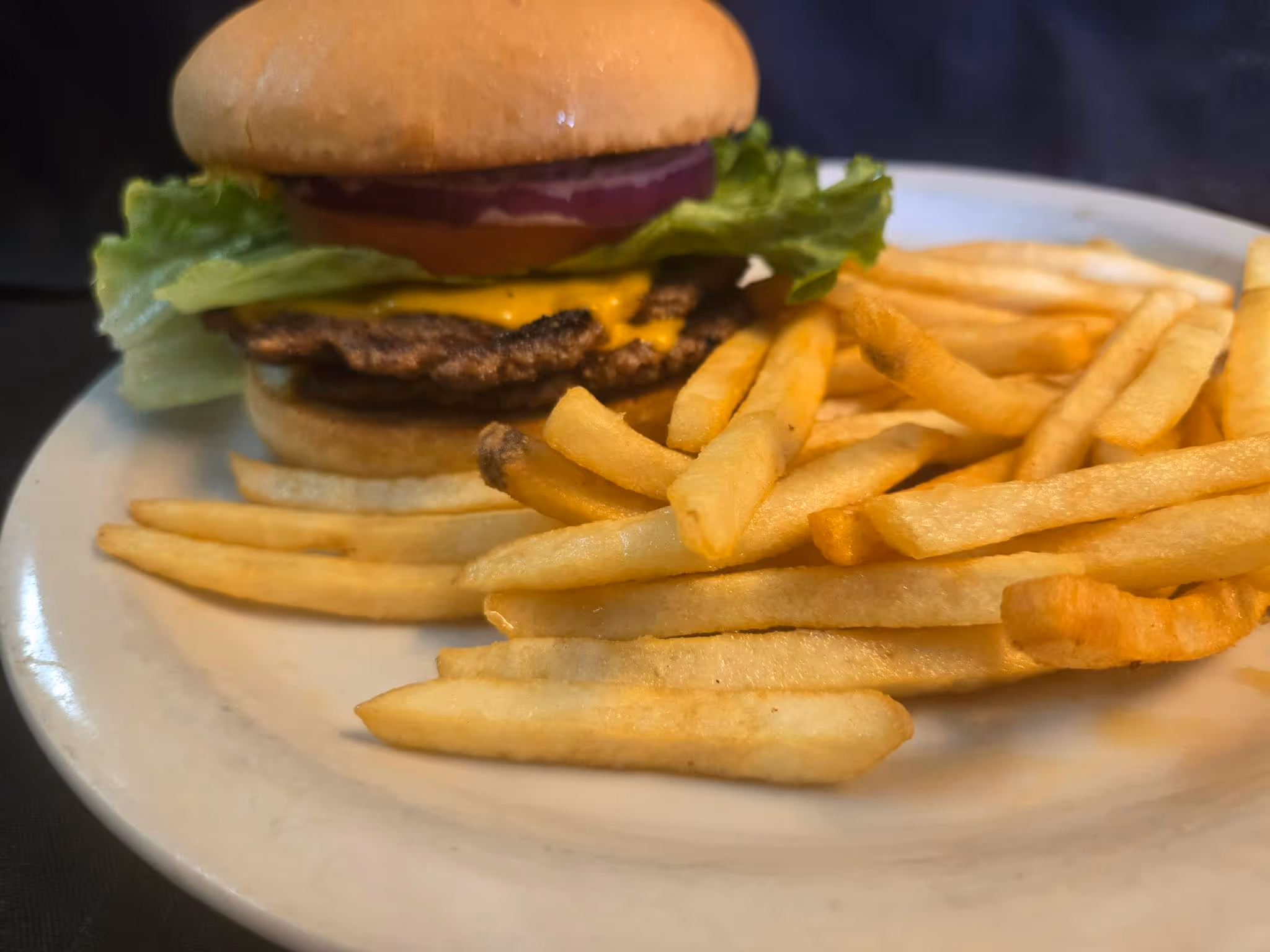 A cheeseburger topped with lettuce and onion sits on a white plate, accompanied by a generous serving of golden French fries.