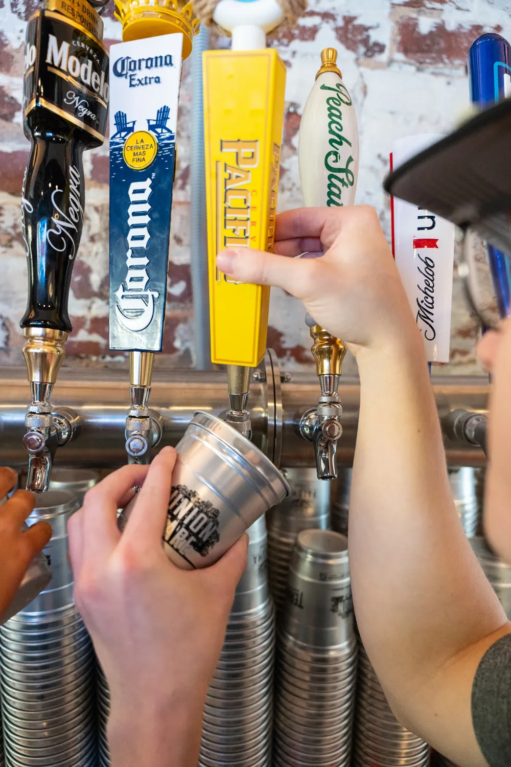 Person pulling Pacifico beer tap handle to pour beer into a metal Union Fare cup at a bar.