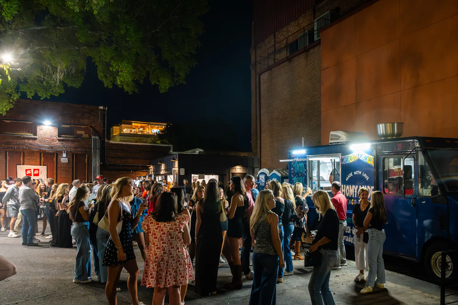 Crowd of people gathered at night outside a blue food truck serving street tacos.