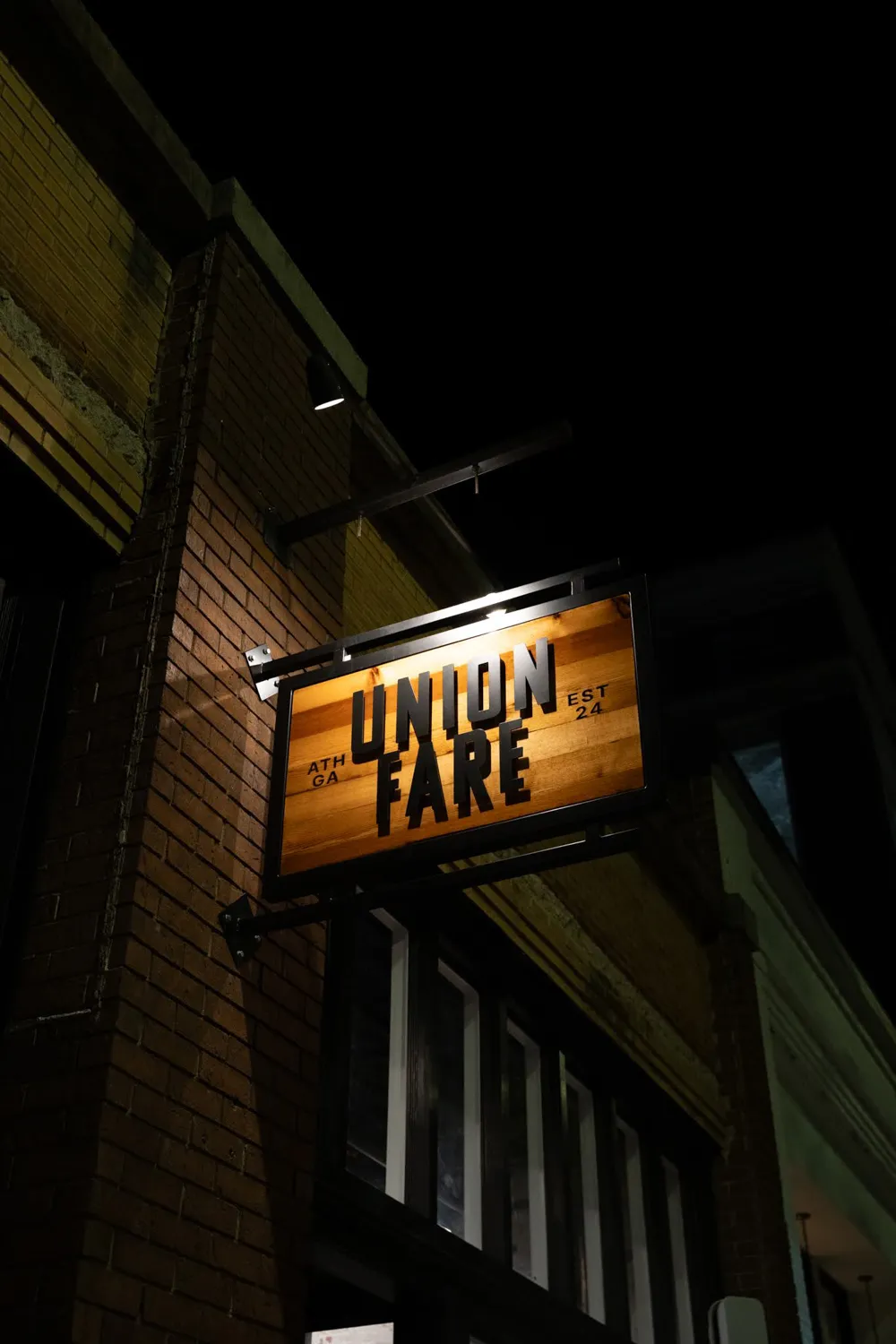 Wooden sign reading 'Union Fare' lit by a spotlight on a brick building at night.