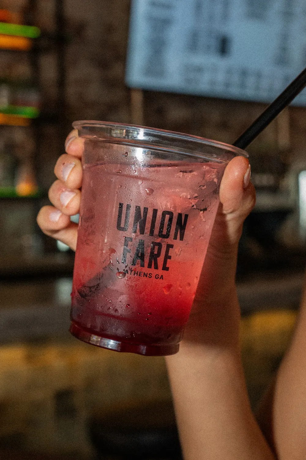 Hand holding a plastic cup with a pink drink and black straw labeled Union Fare Athens GA.