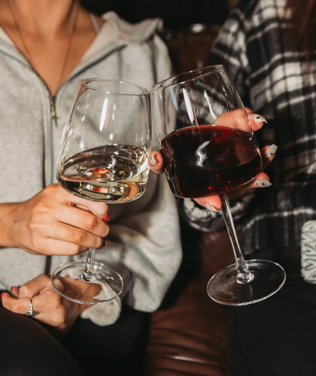 Two people clinking wine glasses, one with white wine and one with red wine.