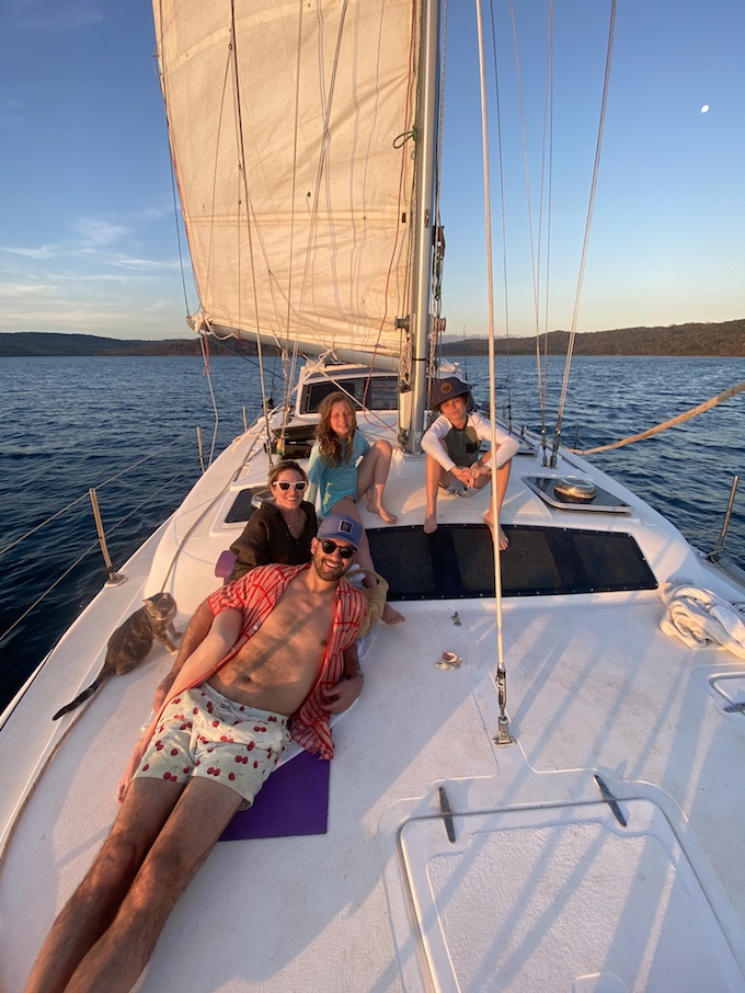 Four people and a cat relaxing on the deck of a private sailboat on calm water during sunset in costa rica
