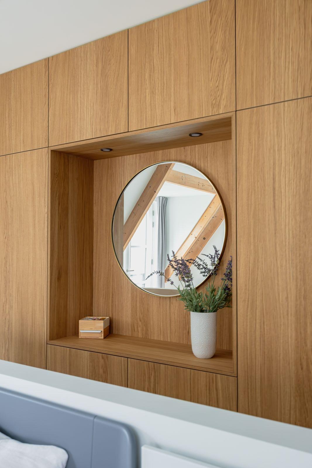 Ingebouwde houten kast met een ronde spiegel, een witte vaas met lavendel en een klein houten doosje.