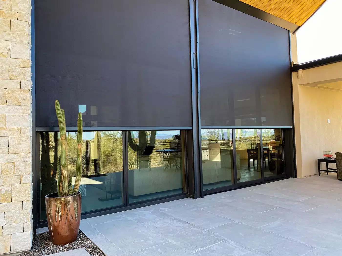 Exterior of a modern house with large black window shades and a potted cactus.