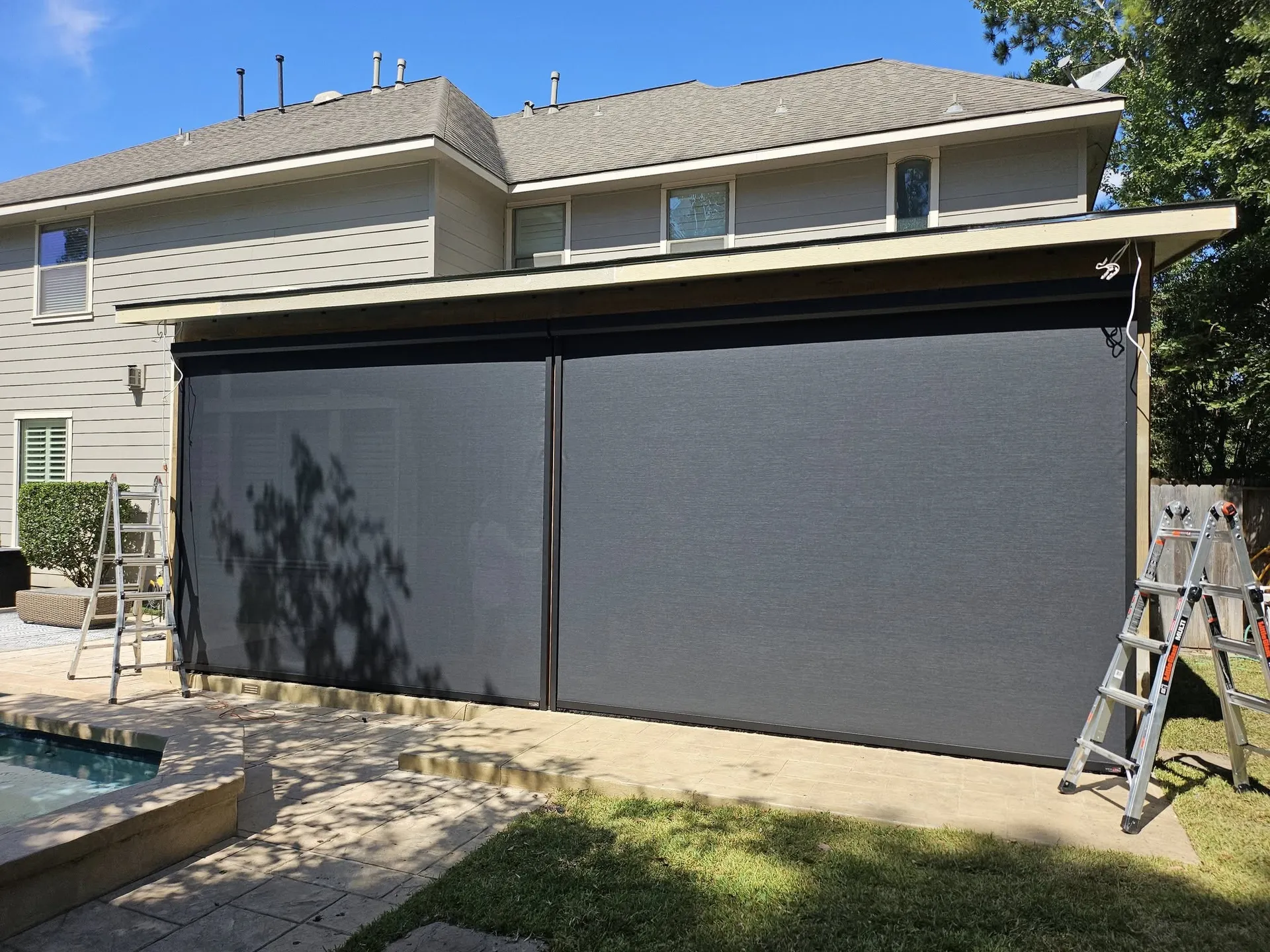 Two large outdoor retractable screens closed on a patio next to a house.