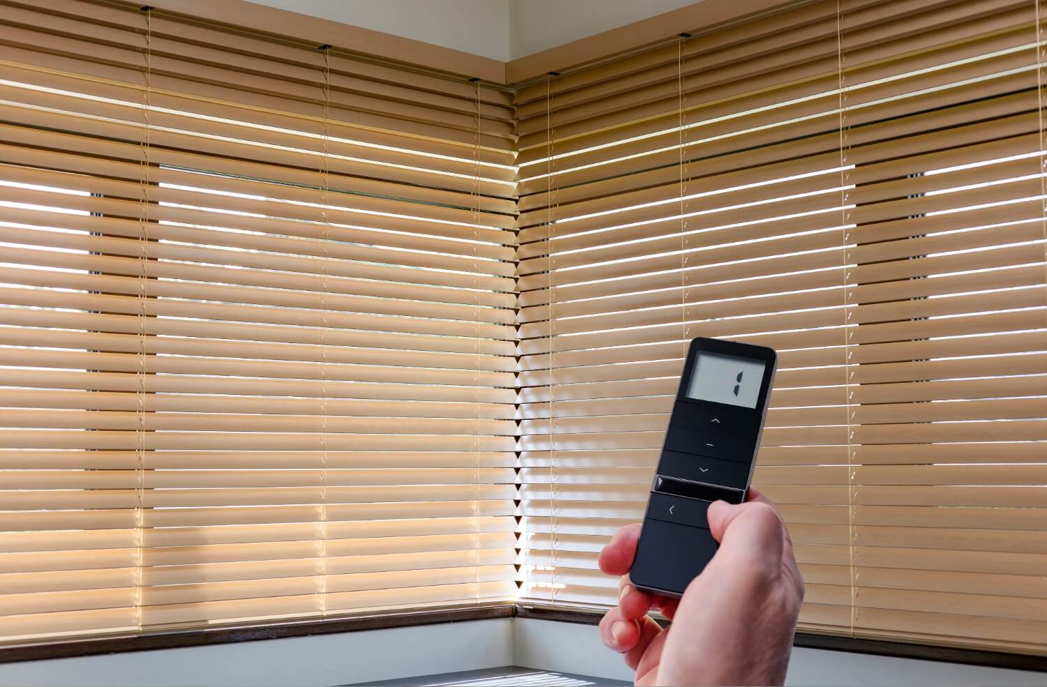 Hand holding a remote control for window blinds.