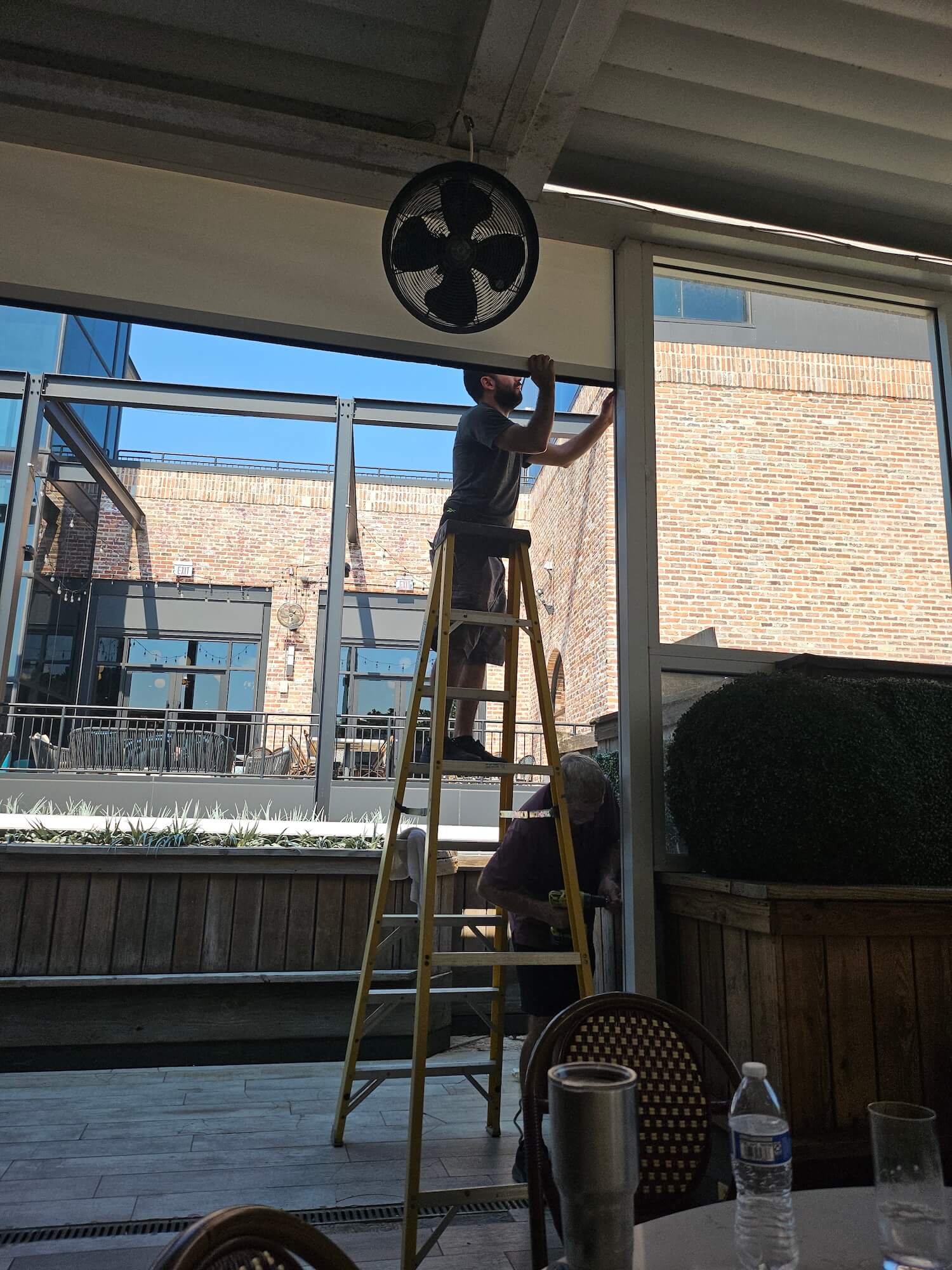 Man on ladder fixing window frame indoors.