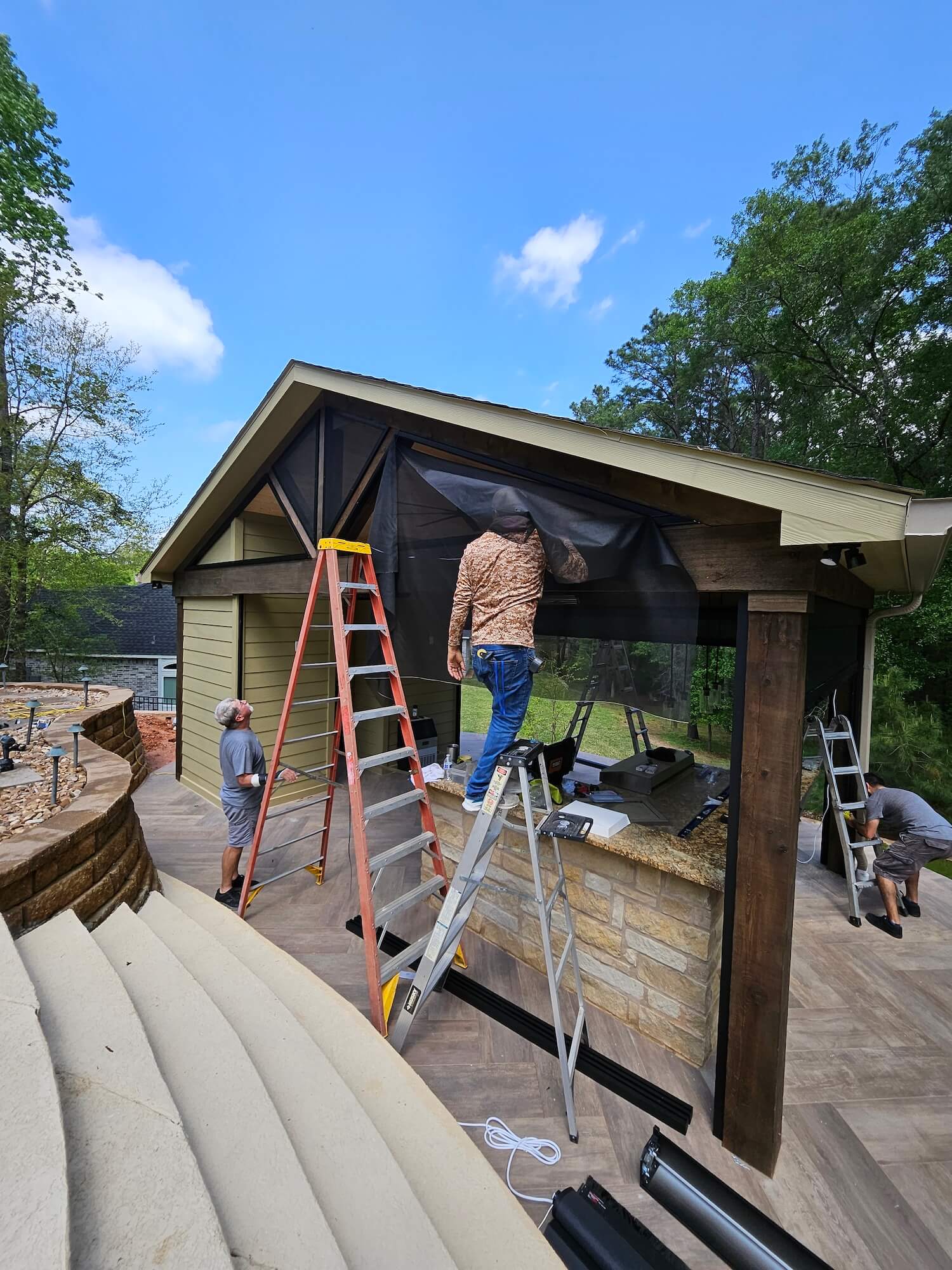 Workers installing a screen on a patio structure using ladders.