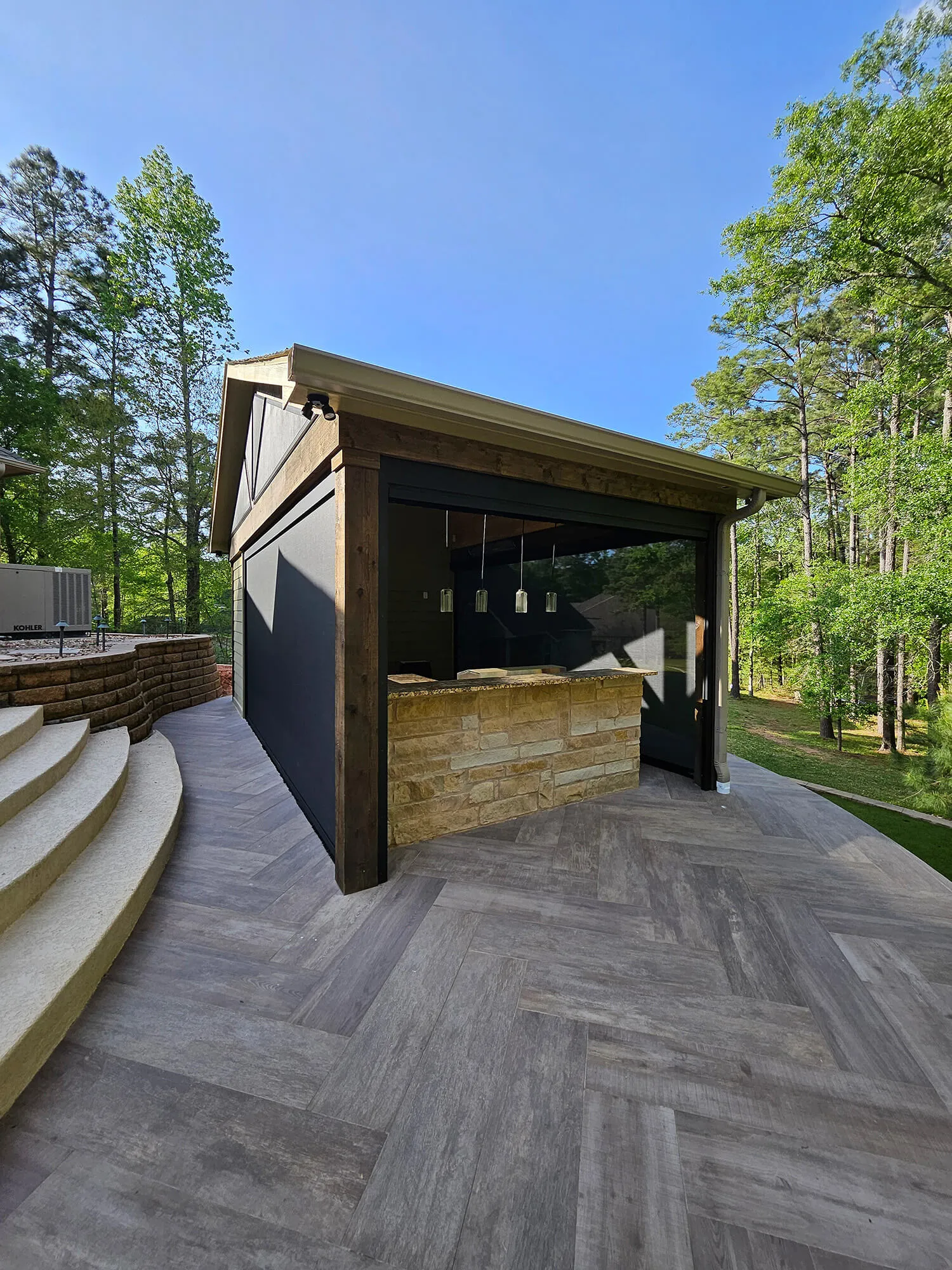 Modern outdoor kitchen with stone bar in wooded setting.