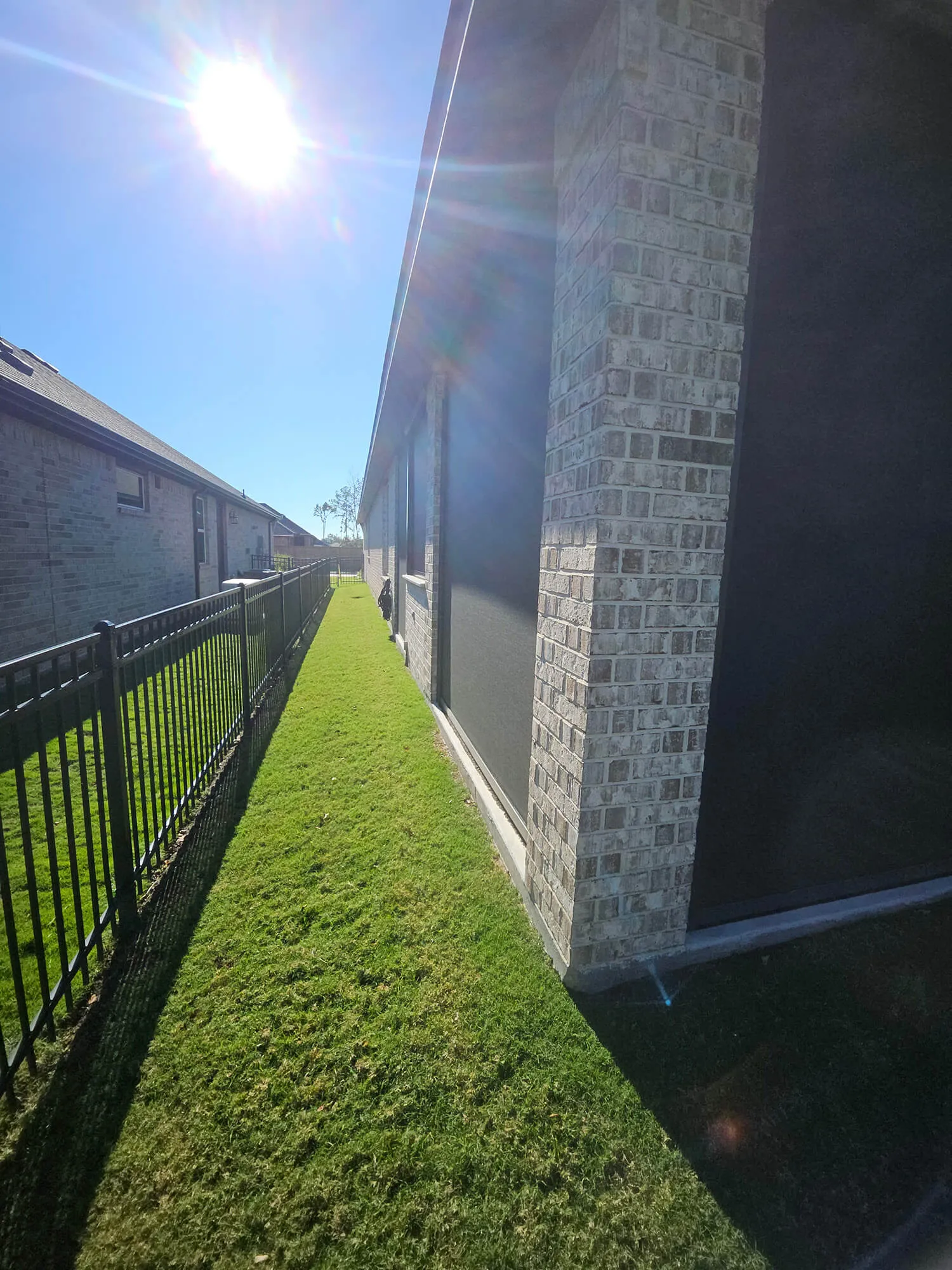 Narrow grassy pathway beside a house under bright sunlight.
