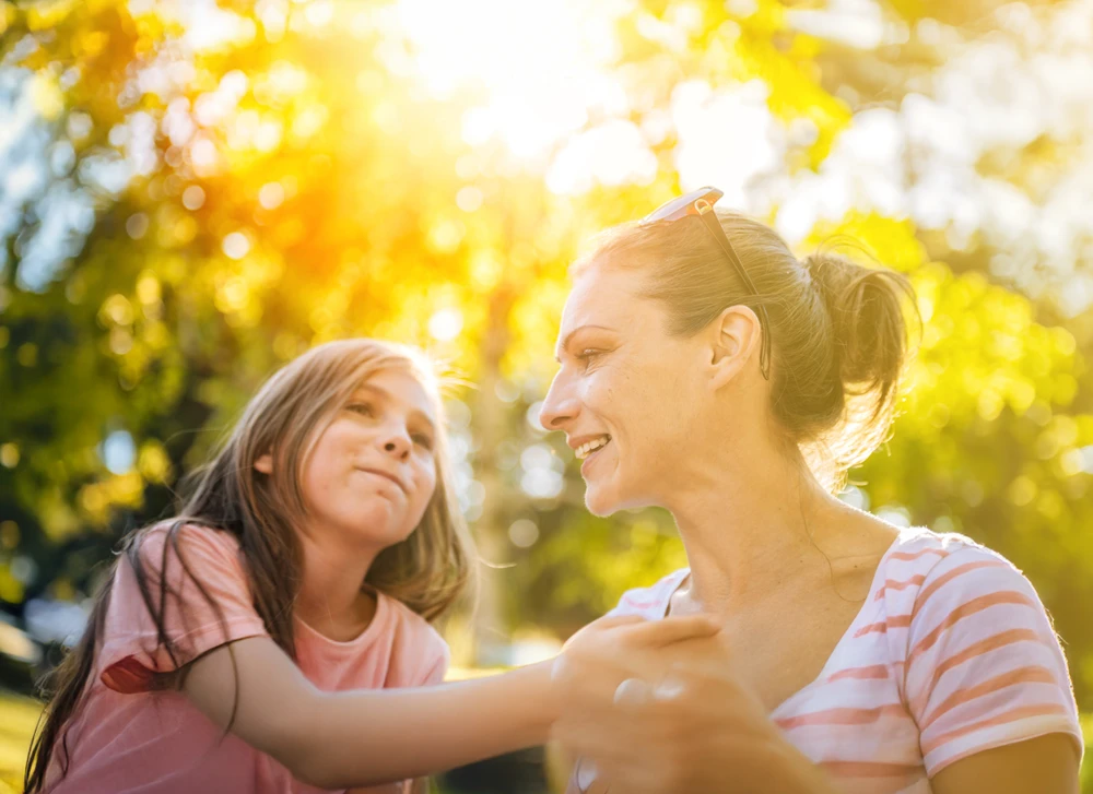 Mother and daughter having a joyful moment with golden sunlight streaming through trees