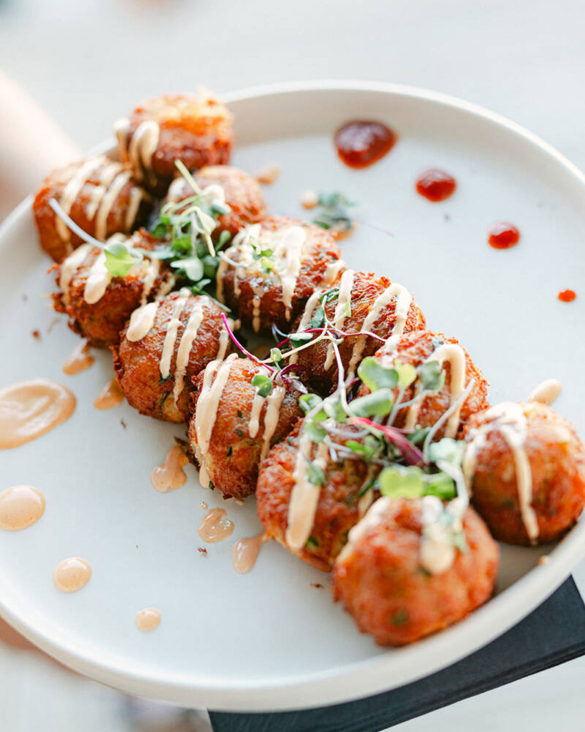 Fried round appetizers drizzled with creamy sauce and garnished with microgreens on a white plate.
