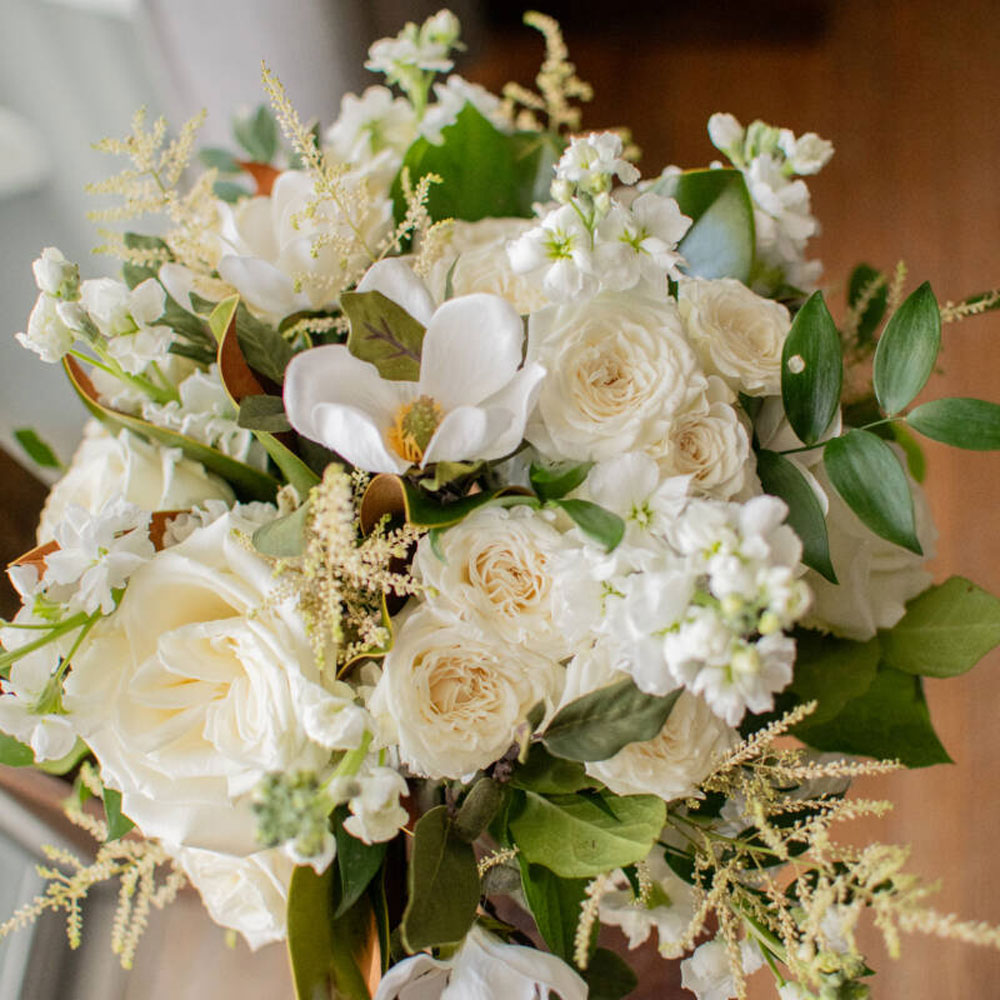 Bouquet of white roses and other white flowers with green leaves and foliage.