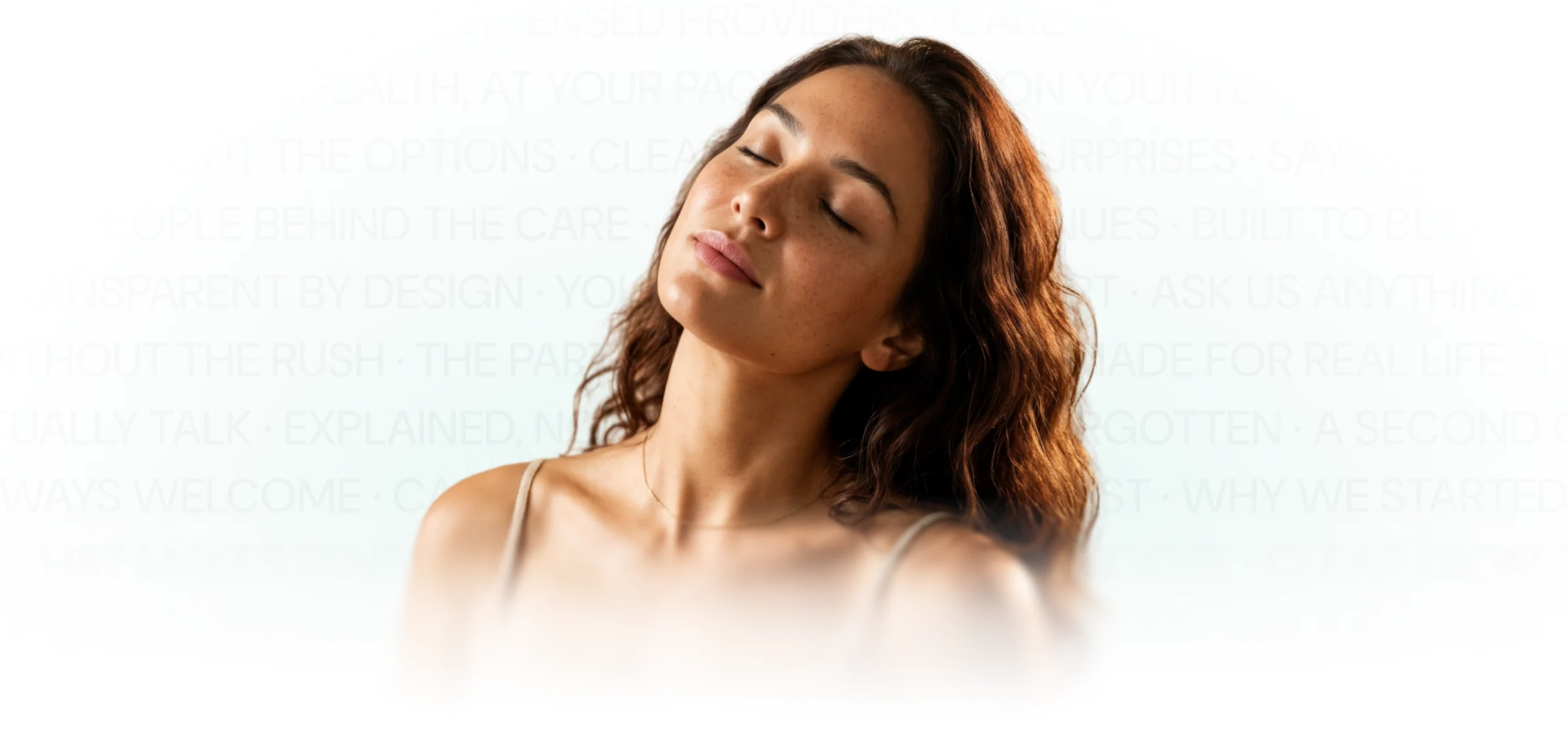 Woman with wavy brown hair and freckles, wearing a beige tank top, tilting her head back with her eyes closed