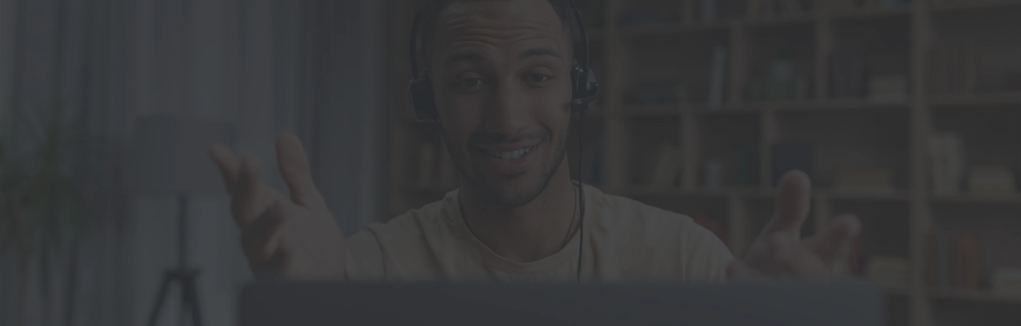 Smiling man wearing headset gesturing during a video call in a room with bookshelves.