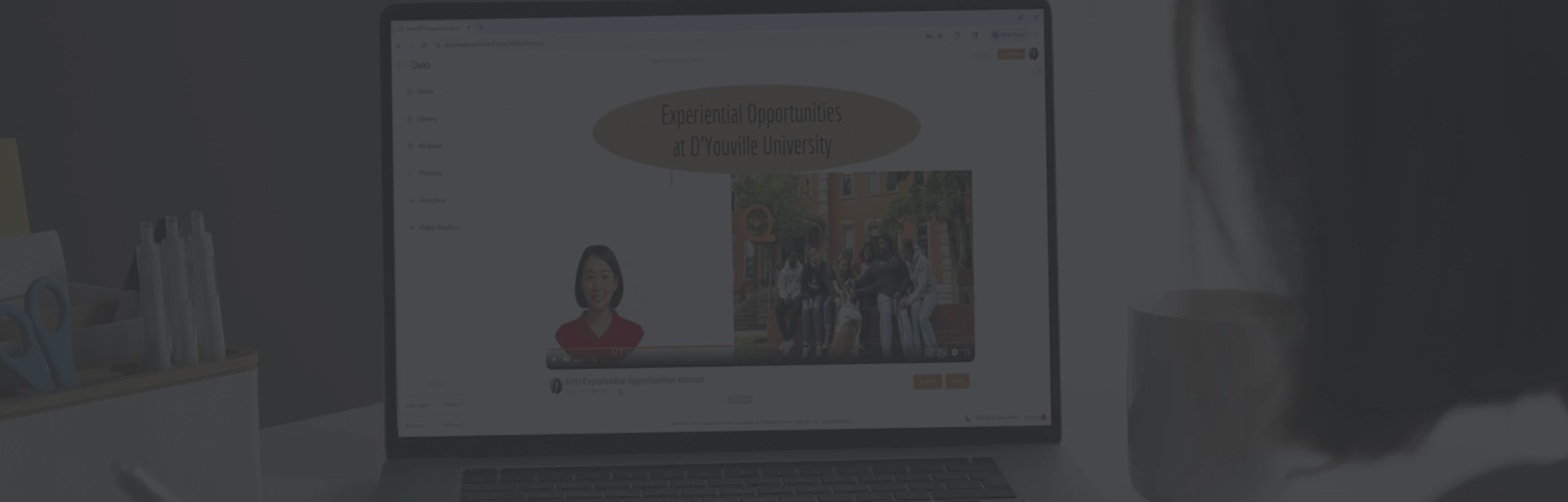 Person viewing a laptop screen showing a video titled 'Experiential Opportunities at D'Youville University' featuring presenters and a group photo.