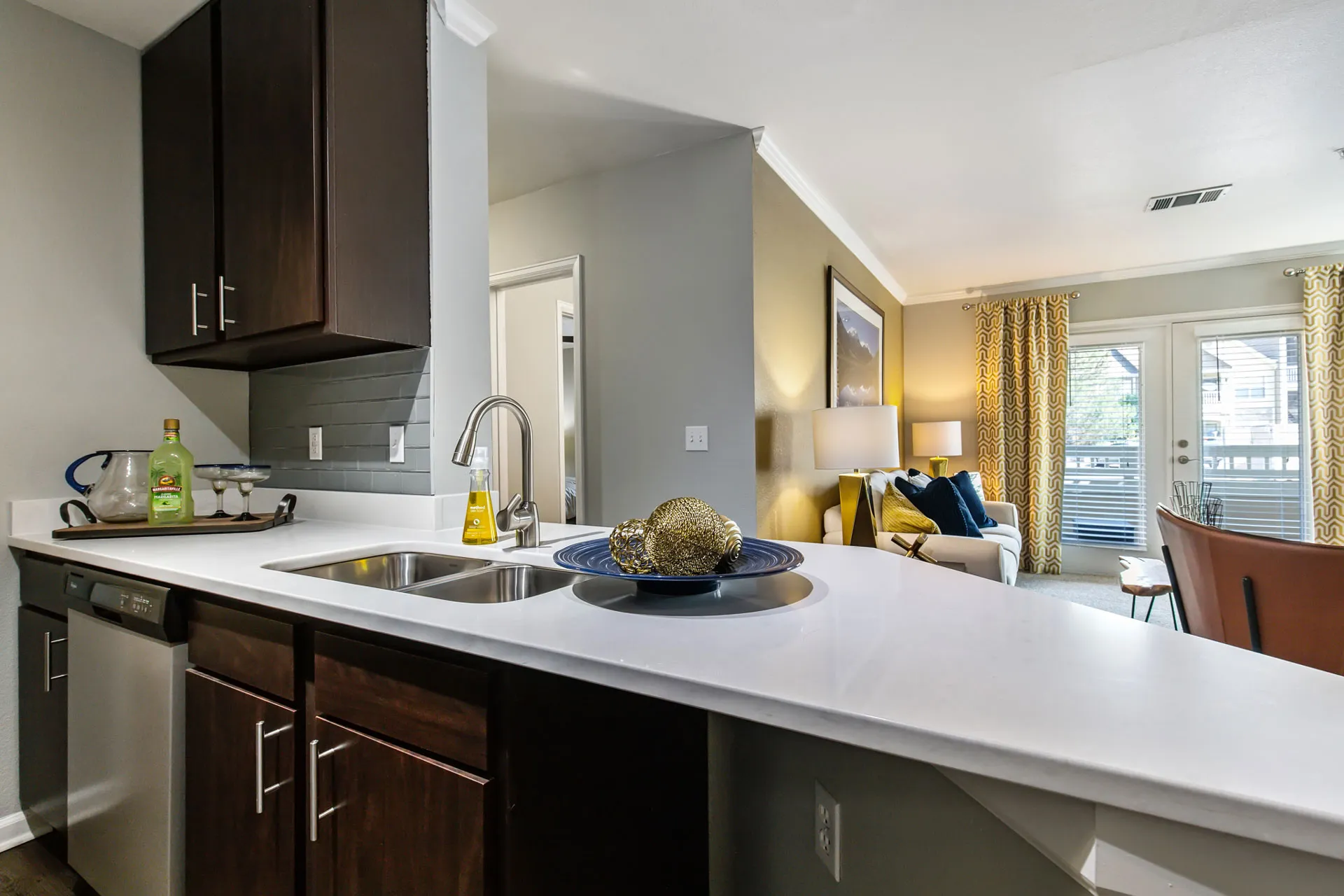 brown cabinets in kitchen with sink, dishwasher, and view into living area with balcony