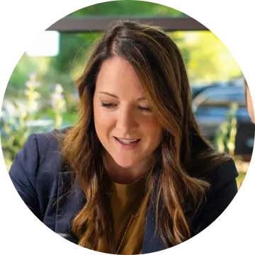 Smiling woman with long brown hair wearing a navy blazer and mustard top outdoors.