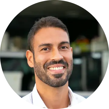 Smiling man with short dark hair and a beard in a white shirt, with a blurred background.