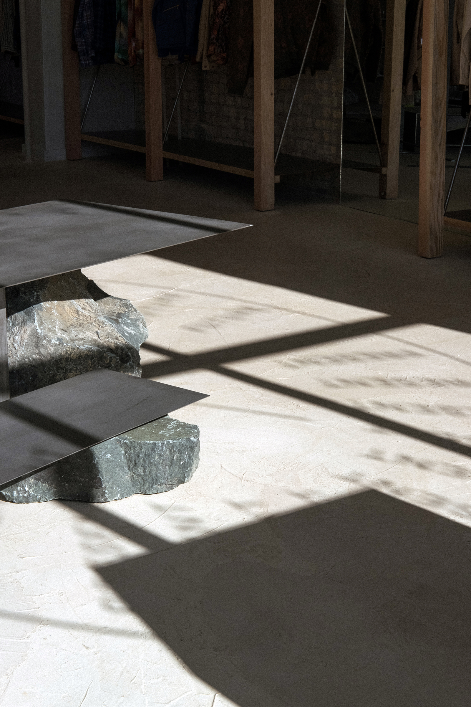 Sunlit minimalist gallery space with concrete benches and wooden support columns casting shadows
