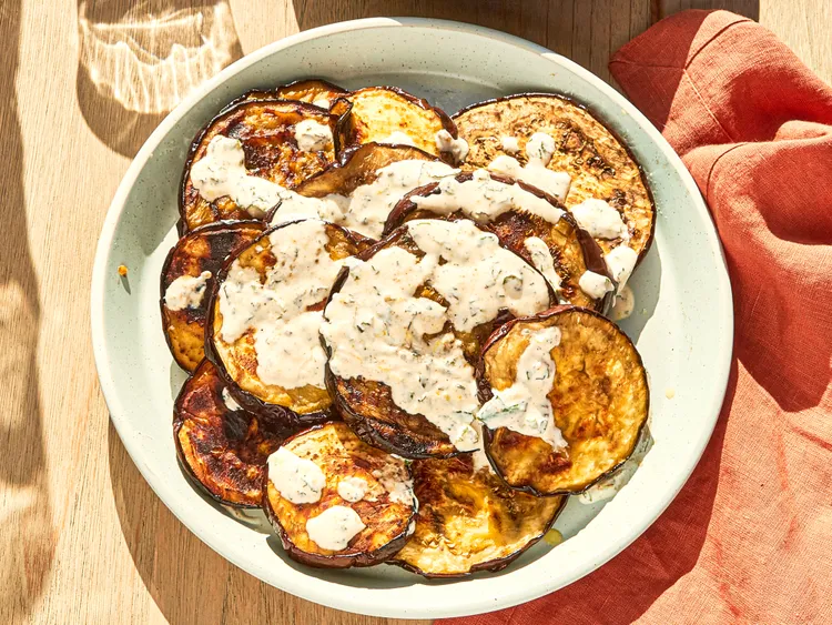 Roasted eggplant rounds topped with garlic yogurt sauce in a bowl