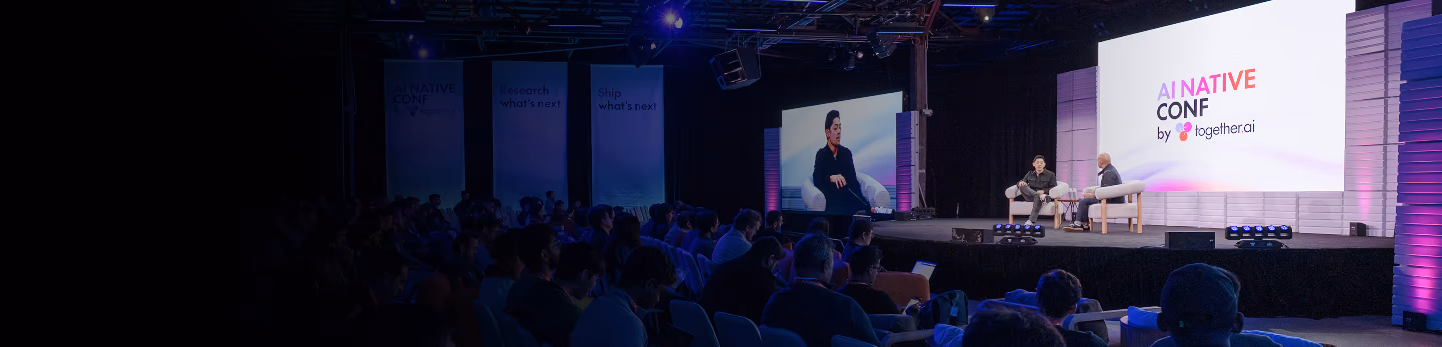 Two speakers seated on stage at the AI Native Conf by together.ai with an audience watching.