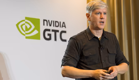 Man speaking at an NVIDIA GTC event, standing next to a logo on a white backdrop.